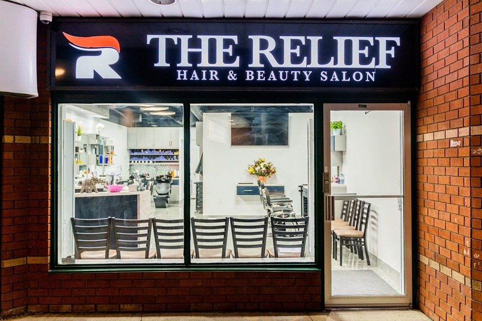 Hair and beauty salon storefront with customer entrance, windows, signage, and waiting chairs