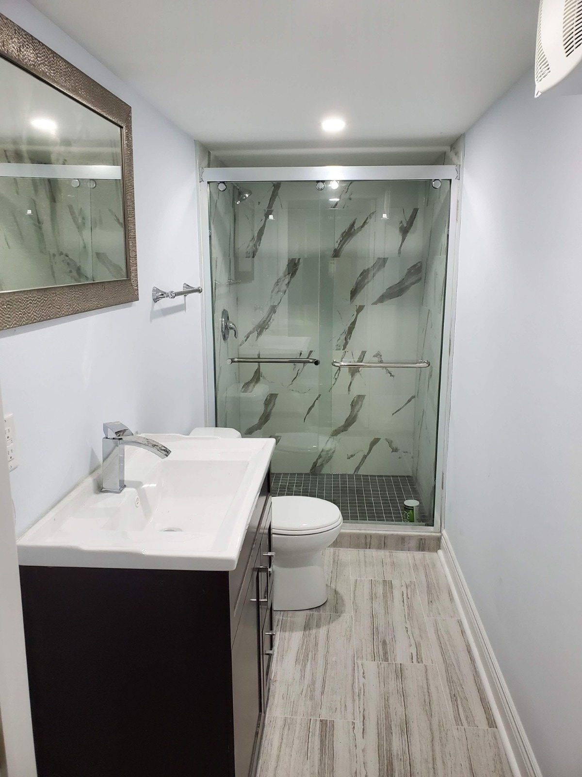 Finished basement bathroom with glass shower enclosure, vanity, mirror, and tile