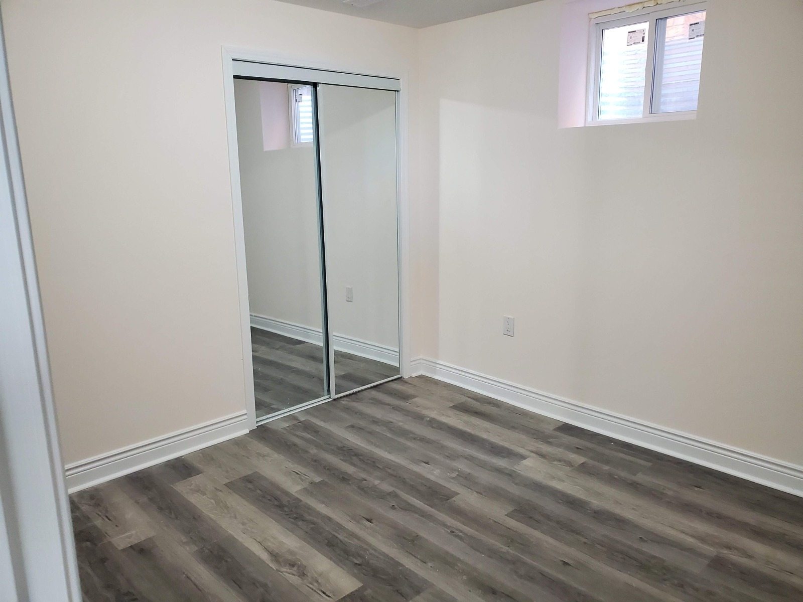 Finished basement bedroom with wood-look flooring, white trim, and mirrored closet doors